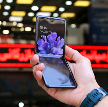 Close-up of a modern flip smartphone held in hand, showcasing innovative technology outdoors in a bustling city.