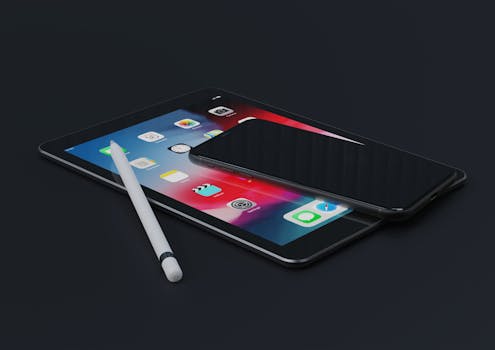 High-angle view of an iPad, iPhone, and stylus on a dark surface, showcasing modern technology.