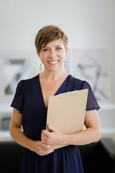 Smiling woman with short hair holding a clipboard, standing indoors.